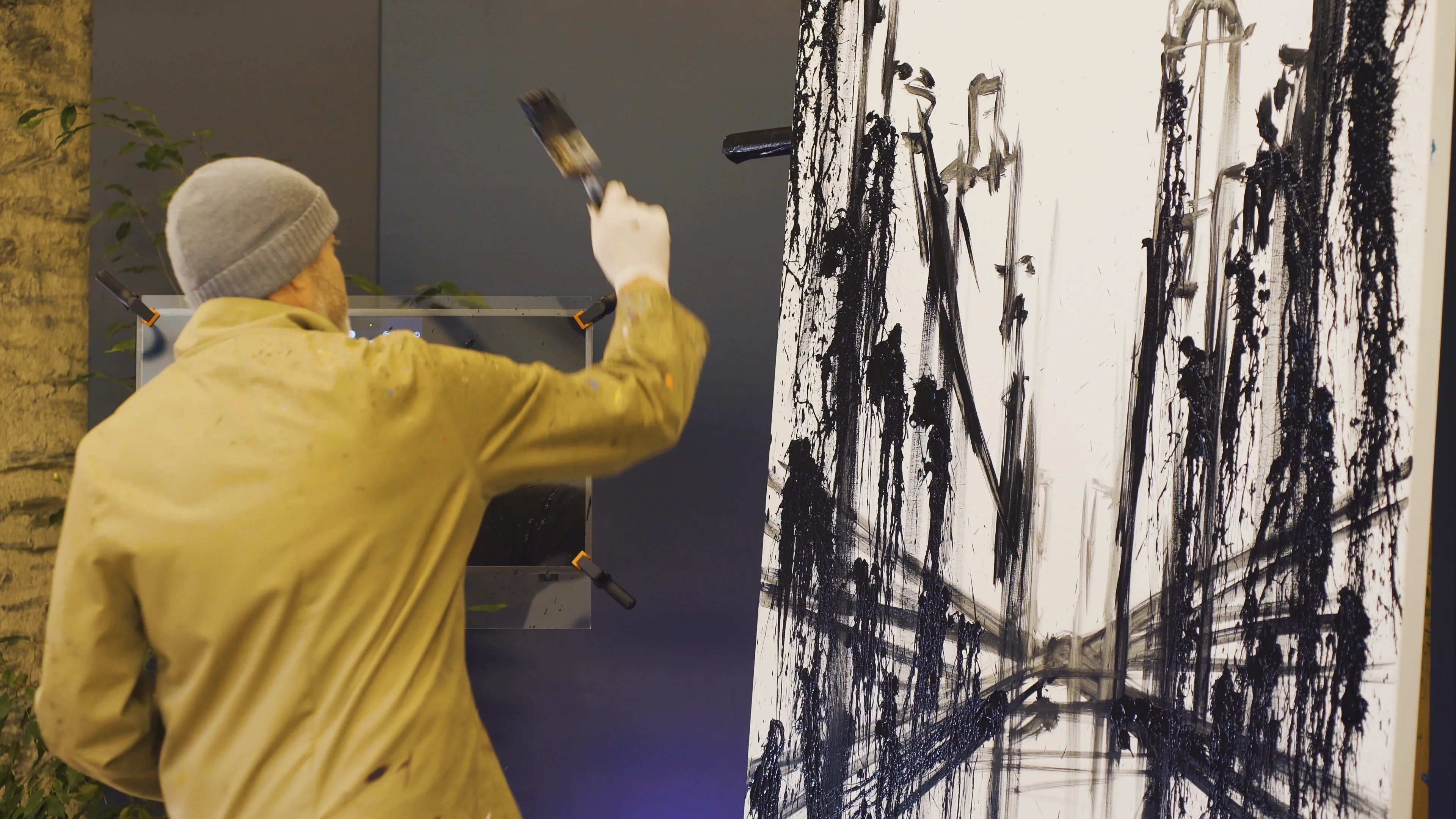 Paul Kenton, brush raised, flicking black paint onto a tall canvas of city streets