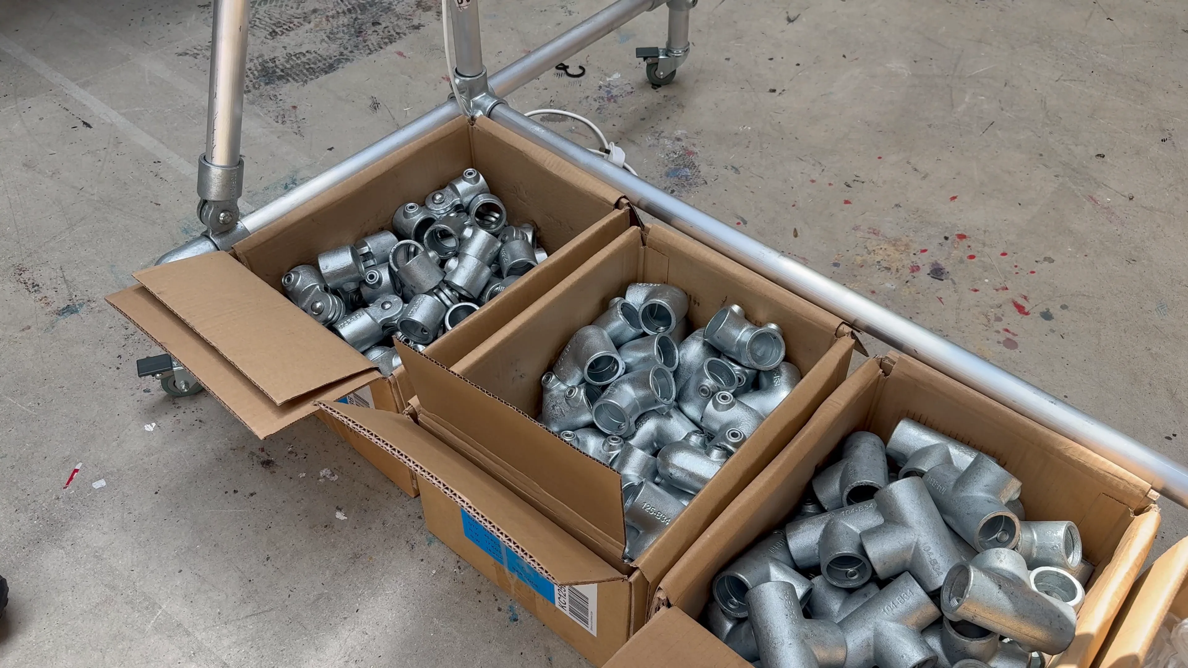 Cardboard boxes full of galvanised steel tube fittings beside a length of scaffold tube on a concrete floor