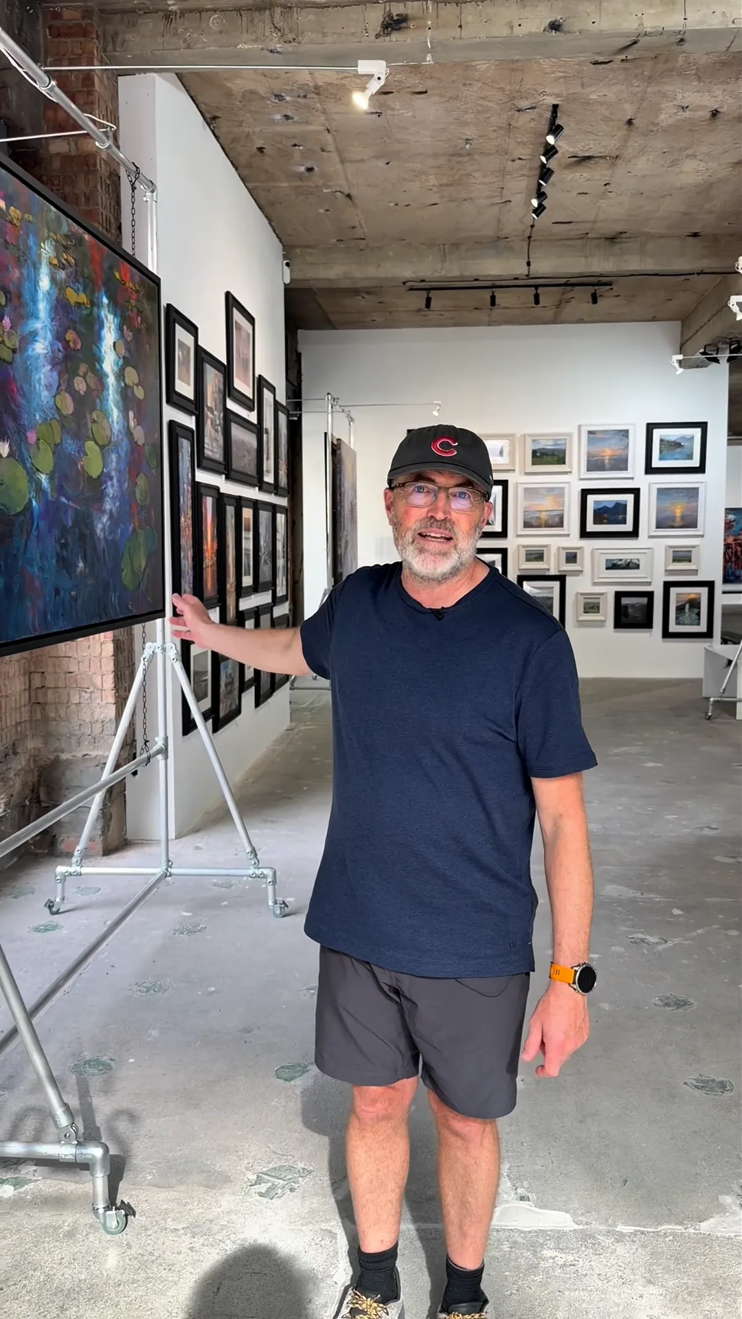 Paul Kenton in a cap and navy T-shirt in the main hall of Urban Echoes, walls of framed paintings behind him